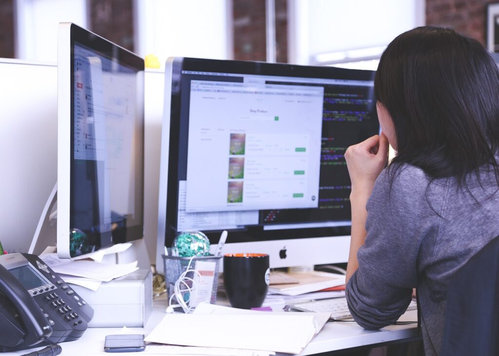 Female employee with her back to the camera sitting at a desk with two large monitors designed for supporting disabled employees with visual impairments